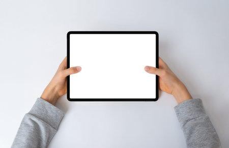 Top view of a kid's hands holding a horizontal tablet on a desk. Flat lay composition with an...