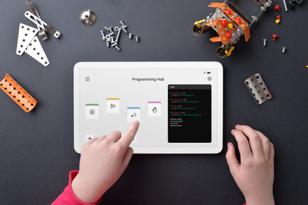 Child programing robot on tablet amidst small parts on work table. Illustrating education,...