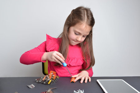 Little girl screws metal parts onto a robot. Concept of hands-on learning, education, creativity, and engineering explorationの写真素材