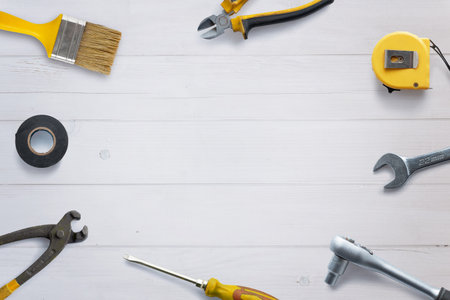 Top view of assorted tools neatly arranged on a white wooden desk, with copy space in the center. Flat lay composition ideal for DIY concept promotionの写真素材