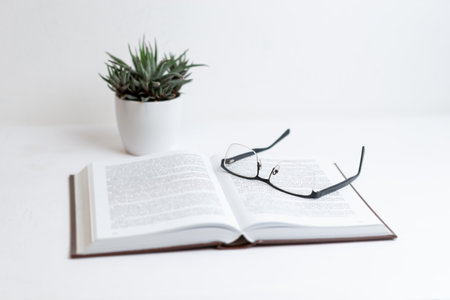 Open book with glasses resting on pages, plant beside. Perfect for relaxation, study, nature, reading time, knowledge, and peaceful learning or academic visualsの写真素材