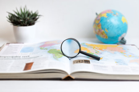 Magnifying glass on open book displaying world map with globe in background. Ideal for themes of global research, travel, geography, exploration, and education visualsの写真素材