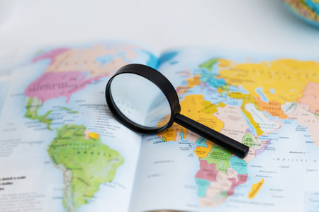Magnifying glass on atlas map, symbolizing travel search, geography exploration, global discovery, and navigation planningの写真素材