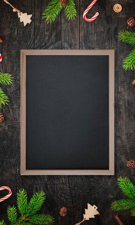 Chalkboard centered on a table surrounded by Christmas tree branches and decorations, featuring an empty surface for writing promotional text in a festive settingの写真素材
