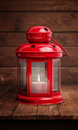 Red lantern with a glowing flame on a rustic wooden table, evoking a romantic Christmas atmosphereの写真素材