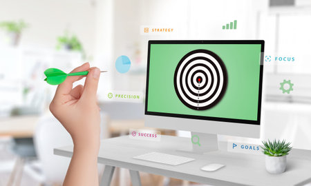 Hand aiming at a display with a target surrounded by floating words like goals, strategy, success,...