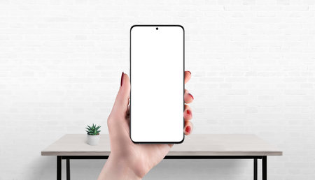 Smartphone mockup in hand with isolated screen, office desk in background, ideal for showcasing app,...