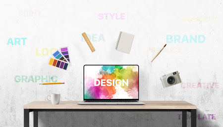 Vibrant design scene with floating art supplies and inspirational keywords on the wall behind a laptop workspace, capturing creative process in motionの写真素材