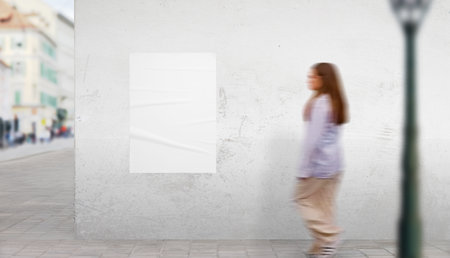 Urban street scene with white poster mockup on building wall. Girl walks by in motion, ideal for dynamic advertising displayの写真素材