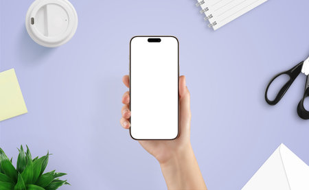 Top view of female hand holding smartphone over creative desk. Ideal mockup for showcasing mobile apps, interface design, or digital toolsの写真素材