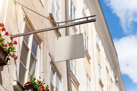 Hanging square shop sign with floral decor and sunny sky, ideal for boutique branding mockups, cafes or local small business advertisementsの写真素材