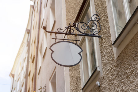 Unique vintage blank signage with wrought iron bracket, perfect for old town shops, cafes, or custom logo mockups in rustic settings.の写真素材