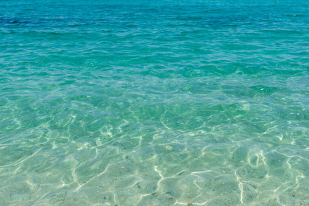 Shallow turquoise sea with sunlight reflections creating mesmerizing patterns on sandy bottom,...