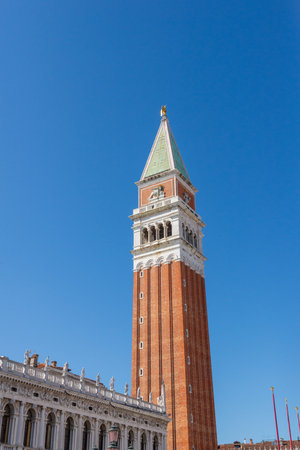 Iconic Venetian tower with red brick and green spire beside historic palaceの写真素材
