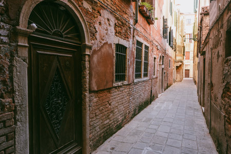 Quiet Venetian alley with old rustic walls, wooden doors, and stone pavement reflecting authentic urban charmの写真素材