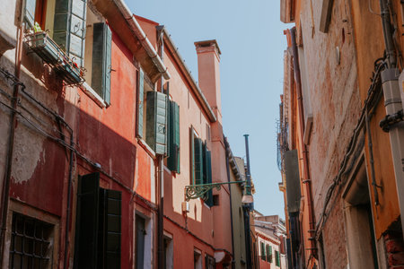 Narrow Venetian street with rustic colorful facades, green shutters, and authentic charm under bright summer skyの写真素材