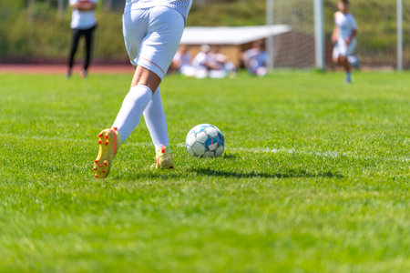 Close-up of young football player in white uniform kicking ball on field.の写真素材
