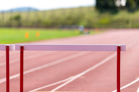 Athletic hurdle standing on red running track with blurred background of green field.の写真素材