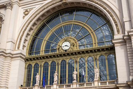 Architectural detail of Keleti Station showing decorative clock, statues, and arched glass window reflecting sky.の写真素材