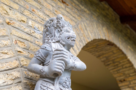 Intricately carved stone statue with fierce expression standing by an arched wall, representing mythological guardian figure in traditional style.の写真素材