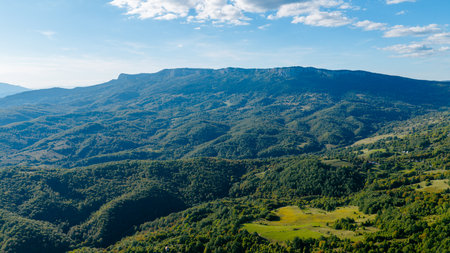 Drone photo showing vast green mountain terrain, forested slopes and open fields in natural daylightの写真素材