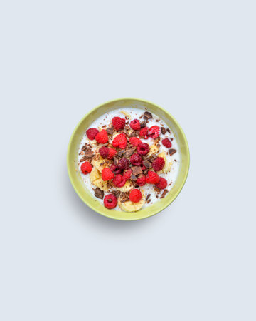 Colorful breakfast bowl with banana, raspberry, chocolate, and yogurt on light background, symbolizing healthy nutrition and morning energyの写真素材