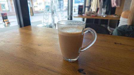 Hot coffee in glass cup on wooden table near bright window inside cafe, modern atmosphere ideal for...