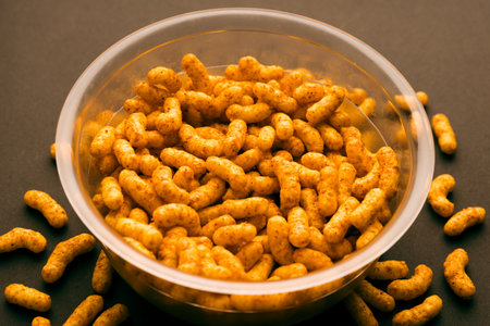 Plastic bowl filled with peanut puff snacks, crispy and golden, ideal for packaging mockups and snack designの写真素材