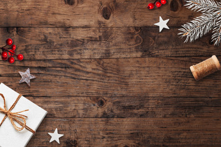 Rustic Christmas wooden background with pine branches, stars, red berries, and festive gift box, natural cozy composition with copy spaceの写真素材