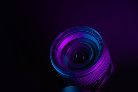 Modern camera lens under purple and blue lighting, futuristic photography equipment background