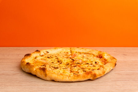 Freshly baked cheese pizza on wooden table with orange background, warm lighting and crispy crust textureの写真素材