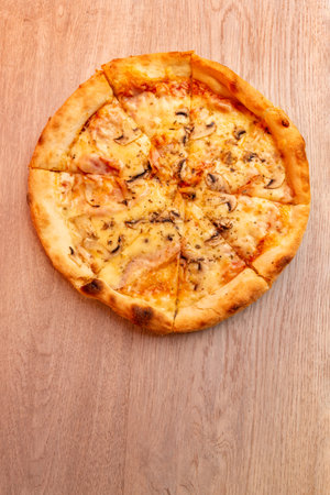 Top view of delicious pizza with melted cheese and mushrooms on wooden table, warm colors and crispy crustの写真素材