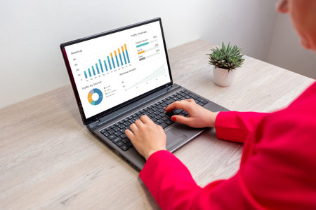 Woman working on laptop analyzing financial dashboard with charts and graphs, concept of data analysis, performance tracking, and business intelligenceの写真素材