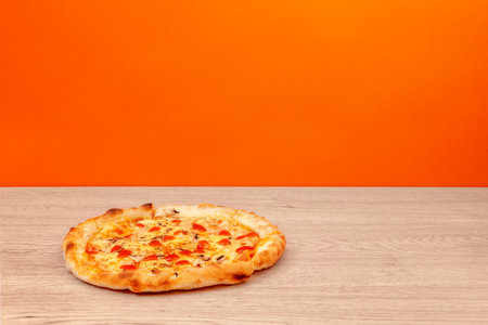Pizza with tomato sauce, cheese, and mushrooms served on light wooden table with vivid orange background.の写真素材