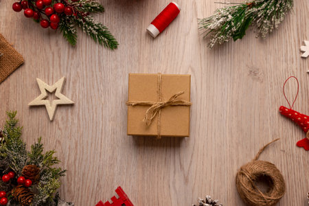 Wrapped gift box with twine on wooden table surrounded by festive elements, ideal for packaging concepts, small business branding and handmade product presentationの写真素材