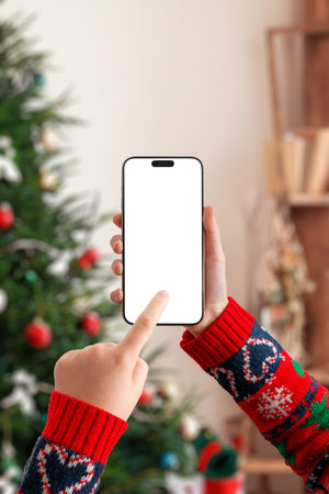 Hand holding smartphone horizontally with blank screen near Christmas tree, perfect for video mockups, streaming apps, holiday marketing and festive UI presentationsの写真素材