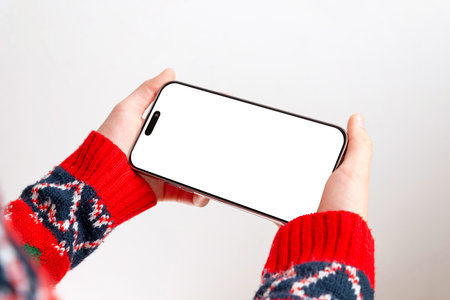 Blank horizontal phone screen mockup with festive sweater sleeves, ideal for app previews, design templates, UI concepts and winter-themed marketing visualsの写真素材