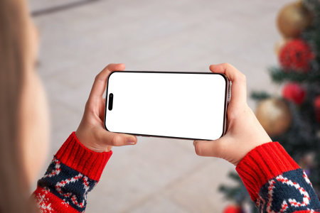 Horizontal phone mockup with festive sweater and Christmas decorations, perfect for holiday designs, winter apps, gaming interfaces and seasonal marketing visualsの写真素材