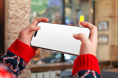 Horizontal phone mockup with gaming hand position in festive urban setting, ideal for winter promotions, holiday visuals, mobile apps and seasonal designsの写真素材