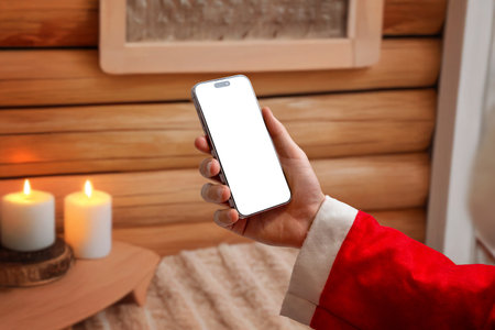 Hand holding smartphone with blank screen in warm Christmas interior, ideal for holiday marketing, festive mockups, mobile app previews and seasonal design projectsの写真素材