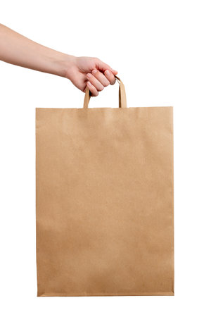Hand holding kraft paper shopping bag on white background, representing eco retail packaging and minimalist commercial designの写真素材