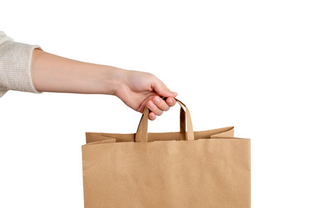 Hand holding kraft paper shopping bag on white background, representing retail purchase, eco packaging and minimalist commercial designの写真素材