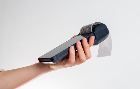 Hand holding portable POS terminal with printed receipt, showcasing mobile payment technology in a clean minimal retail settingの写真素材