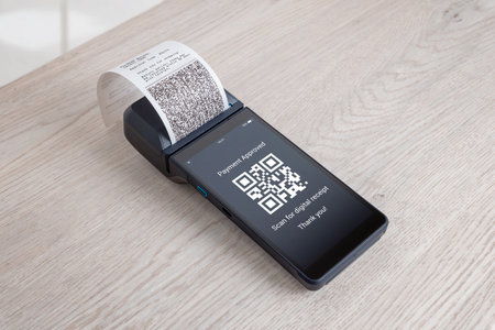 odern POS terminal with printed receipt and QR code displayed on screen during approved digital payment on a clean wooden surfaceの写真素材
