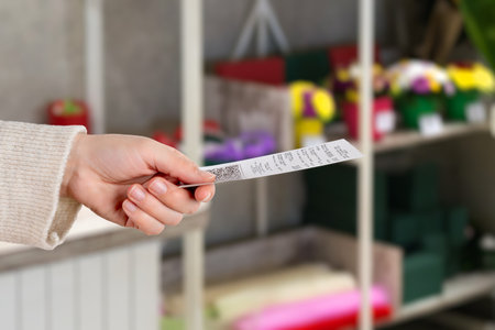 Hand holding printed retail receipt with QR code inside flower shop, showing purchase confirmation and modern checkout experienceの写真素材