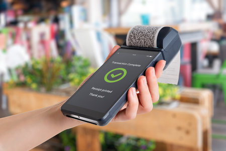 Hand holding POS terminal in store environment, showing completed payment with green checkmark and printed receipt during retail checkoutの写真素材