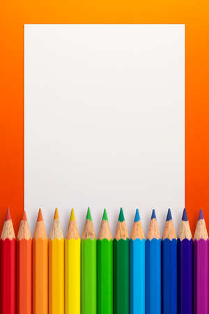 Vertical frame made of color pencils and white paper on an orange background.の写真素材