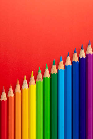 Colour pencils arranged diagonally on a red vertical paper background.の写真素材
