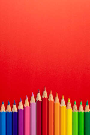 Creative vertical background made of colour pencils on red paper. Flat lay. Education concept.の写真素材