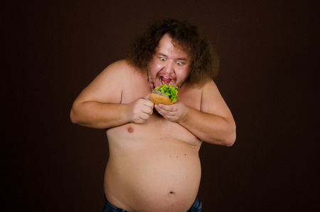 Hungry naked man eating a hamburger.の写真素材